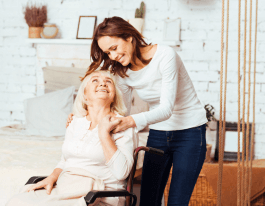 Joyful delighted old women sitting in wheelchair and lookign at her caregiver