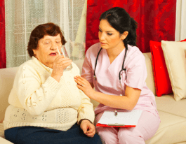 Nurse assisting an elderly woman drinking water at home