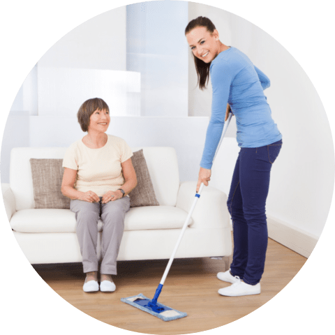 Portrait of caretaker cleaning floor with mop while senior women sitting on sofa at nursing home