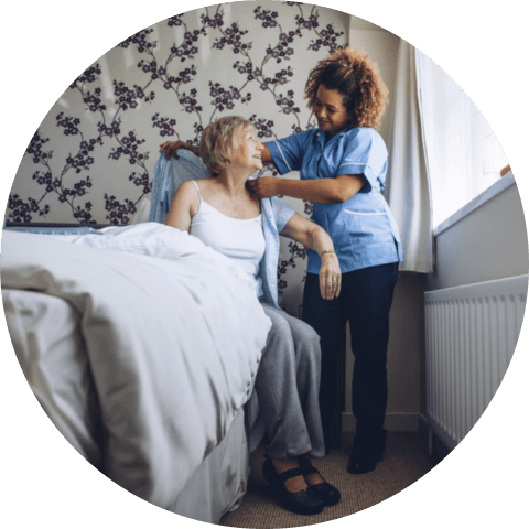 Caregiver helping a senior women get dressed in her bedroom